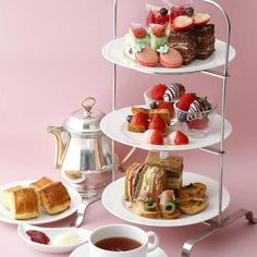 three tiered trays filled with sandwiches and pastries next to a cup of tea