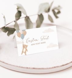 a white plate topped with a card next to a green leafy plant and a brown teddy bear