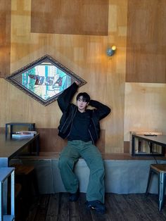 a young man sitting on a bench in front of a wooden wall with a mirror above it