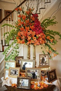 an arrangement of flowers and framed pictures on a table in front of the stair case