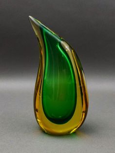 a green and yellow glass vase sitting on top of a table next to a gray wall