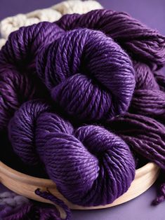 several skeins of purple yarn in a wooden bowl on a purple tablecloth