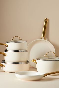 a set of white pots and pans with gold handles sitting on a counter top