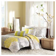 a bed with yellow and gray comforters in a room next to a window,