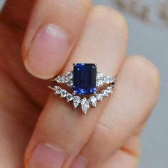 a woman's hand holding an engagement ring with a blue stone surrounded by diamonds