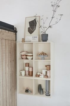 a shelf filled with vases and other items on top of a wall next to a wooden door