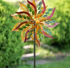 a colorful wind spin sitting on top of a metal pole next to a lush green field