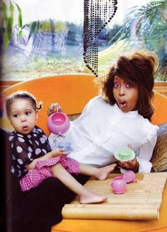 two women sitting on a yellow couch with cups and teapots in their hands