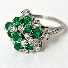 Beautiful Vintage 18 kt white gold cluster ring carrying round diamond cut emeralds and brilliant cut diamonds set in a free pattern. The two colors are wonderfully balanced in this piece, making the ring very unique. The quality of the stones is very high. The top measures 16x18 mm and raised to 11.5 mm height from a finger. Rounded shank is 1.5 mm wide on the bottom and on the top splits into three wires to 3.5 mm wide. The ring is size 7 and weighs 5.2 grams. 10 round diamond cut genuine no t White Gold Emerald Ring With Brilliant Cut Cluster, Green Cluster Diamond Ring, White Gold Cluster Emerald Ring With Brilliant Cut, Classic Cluster Emerald Diamond Ring, Cluster Diamond Emerald Ring, Classic Cluster Emerald Ring With Prong Setting, Cluster Emerald Ring In White Gold With Center Stone, Cluster Emerald Ring With Diamond Center Stone, Cluster Emerald Ring With Diamond