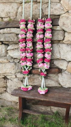 pink and white flowers are hanging from the side of a stone wall next to a bench