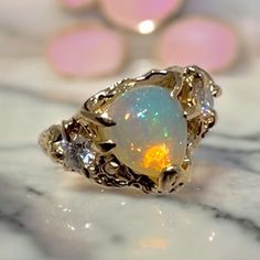 This stunning ring is made of 14k solid gold and has a pear shape high quality natural fire opal that captures attention with its mesmerizing play of colors. On each side of the opal, there are two brilliant cut Moissanites, adding a touch of elegance and sparkle. The design of the ring features organic shapes, giving it a unique and artistic feel. The shiny finish of the gold enhances its beauty and makes it stand out even more. This ring is truly one of a kind, with its sea life-inspired desig 14k Gold Multi-stone Opal Ring, Unique Untreated Ring Jewelry, Unique Multi-stone Promise Rings, Unique Pear-shaped Gold Jewelry, Unique Yellow Gold Emerald Promise Ring, Unique Opal Gemstone Rings, Unique Yellow Gold Opal Ring For Anniversary, Unique Gold Opal Ring With Multi-stone, Untreated Fine Jewelry For Anniversary