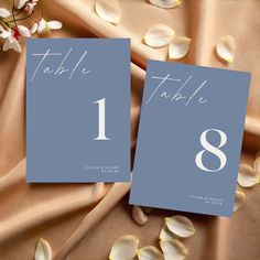 two cards with the number one on them are sitting next to flowers and petals in front of a cloth background