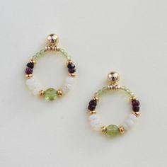 Our white opal, ruby, and peridot earrings are packed with gemstones.  A unique July, August or October birthstone gift OR 14th, 15th, 16th or 40th-anniversary gift.  The 14k gold-filled post earrings feature a peridot bead at the base and top of the hoop, complemented by white opals, gold-plated brass, and contrasting red rubies.  The pair is lightweight and long-lasting.  A lovely personal treat or gift for your wife, mom, or friend.   The jewelry arrives wrapped for easy gifting and includes Gemstone Accented Earrings For May Birthstone, May Birthstone Earrings With Natural Stones For Gift, Small Hoop Birthstone Earrings For Anniversary, Dainty Hoop Earrings With May Birthstone, Natural Stone Earrings For May Birthstone Gift, Dainty May Birthstone Hoop Jewelry, May Birthstone Hoop Gemstone Jewelry, May Birthstone Earrings With Gemstone Accents, May Birthstone Earrings With Natural Stones