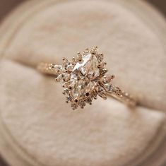 an engagement ring sitting on top of a white cloth covered box with a diamond in the center