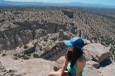 a woman sitting on top of a large rock next to a valley filled with trees