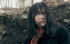 a man with long black hair standing in the dirt