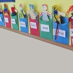 a row of colorful bags with name tags on them hanging from the side of a wall