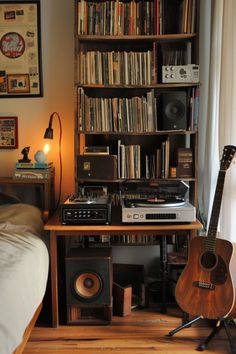 a room with a bed, bookshelf and guitar on the floor in front of it