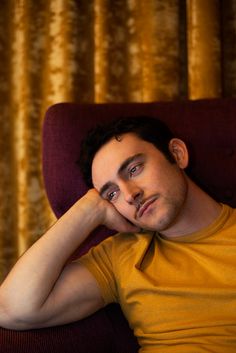 a man sitting in a red chair with his hand on his chin looking at the camera