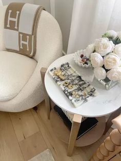 a white chair sitting next to a small table with flowers on it and a book