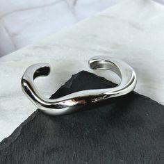 This unique bangle bracelet is designed to make waves and add a bold touch to any outfit. Size: One Size Material: Stainless Steel Plating: Silver Bracelet is 100% nickel-free and cadmium-free Bracelet is hypoallergenic and tarnish resistant Trendy Tarnish Resistant Cuff Bracelet Bangle, Adjustable Cuff Bracelet With Polished Finish, Trendy Adjustable Jewelry With Polished Finish, Adjustable Tarnish Resistant Silver Cuff Bracelet, Modern Tarnish Resistant Cuff Bracelet, Adjustable Modern Bangle Tarnish Resistant, Adjustable Wavy Bracelets As Gift, Modern Adjustable Tarnish Resistant Bangle, Adjustable Bangle With A Modern Twist As A Gift