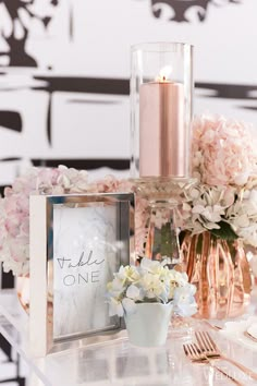 a table topped with flowers and a vase filled with pink hydrangeas next to a candle