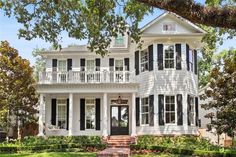 a large white house with black shutters on the front and second story, surrounded by trees