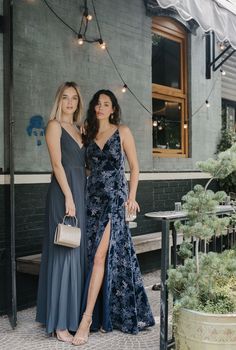 two women standing next to each other in front of a building with lights hanging from the ceiling