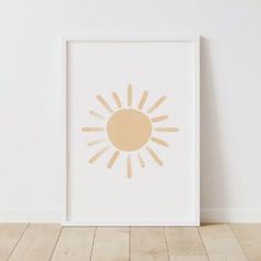 a white frame with a yellow sun print on the wall in front of a wooden floor