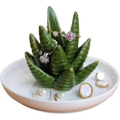 a white plate topped with lots of green plants next to earrings and rings on top of it