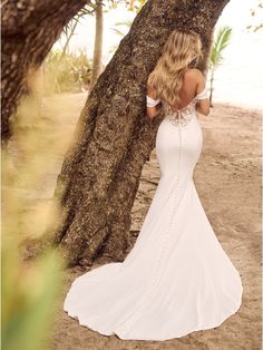 a woman standing next to a tree wearing a white dress with beading on the back