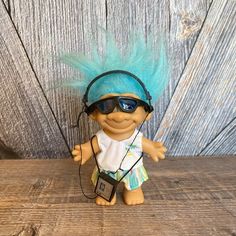 a troll doll with blue hair wearing headphones and listening to music on a wooden surface