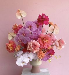 a vase filled with lots of different colored flowers on top of a white table next to a pink wall