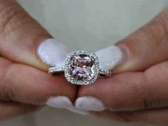 a close up of a person's hands holding a ring with a pink diamond