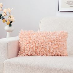 a pink pillow sitting on top of a white chair next to a vase with flowers