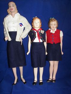 three dolls standing next to each other in front of a blue background and one is wearing a skirt