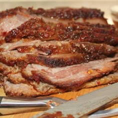 sliced meat sitting on top of a wooden cutting board next to knifes and fork