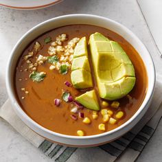 a bowl of soup with avocado on top and corn in the middle next to it