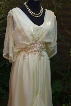 Here is my buttercream chiffon and satin draped evening dress, inspired by the elegant style of the 20s and 70s. This unique design is perfect for romantic weddings, proms, or any special occasion. The dress features delicate, silky buttercream chiffon that drapes beautifully and is fully lined with ivory satin for a luxurious and comfortable feel. It's beautifully finished with gold embroidery, gold beading, faux pearls, and vintage lace accents, adding a touch of glamour and vintage charm. . T Luxury Vintage Dress For Costume Events, Luxury Romantic Vintage Costume Dress, Luxury Lace Bodice Dress For Vintage Events, Luxury Romantic Cream Gown, Luxury Vintage Dress With Ruched Bodice, Luxury Romantic Victorian Dress For Vintage Events, Luxury Cream Elegant Evening Dress, Luxury Elegant Cream Evening Dress, Luxury Romantic Cream Dress