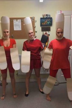 three women in red shirts and white paper hats are holding up large pieces of cardboard