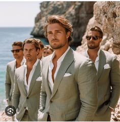 a group of men in suits standing next to each other near the ocean and rocks