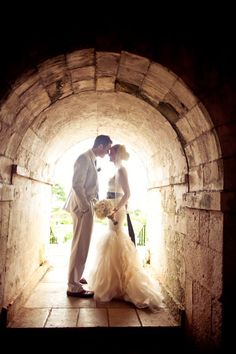 a bride and groom are kissing in an old stone tunnel with sunlight coming through the window