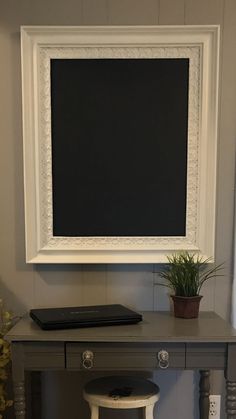 a small desk with a potted plant and a chalkboard on the wall above it