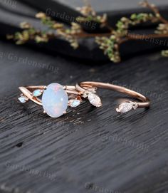 an opal and diamond ring sitting on top of a wooden table next to a twig