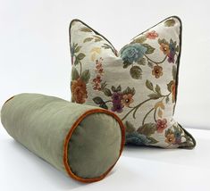 two pillows and a rolled pillow on a white surface with floral print, one is green