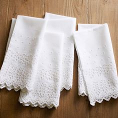 three white embroidered napkins on top of a wooden table