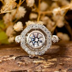 a diamond ring sitting on top of a piece of wood with flowers in the background