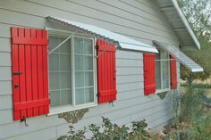 red shutters on the side of a house with flowers growing in front of it