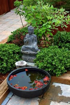 a buddha statue sitting in the middle of a garden with water and plants around it