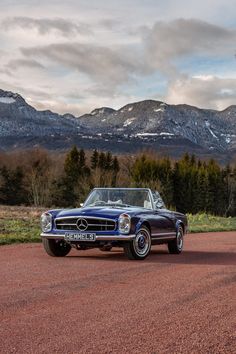 an old car is parked on the side of the road in front of some mountains